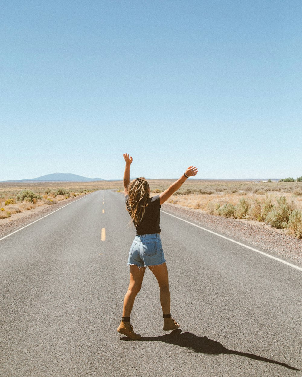 Mujer con camiseta sin mangas negra y pantalones cortos de mezclilla azules corriendo en la carretera durante el día