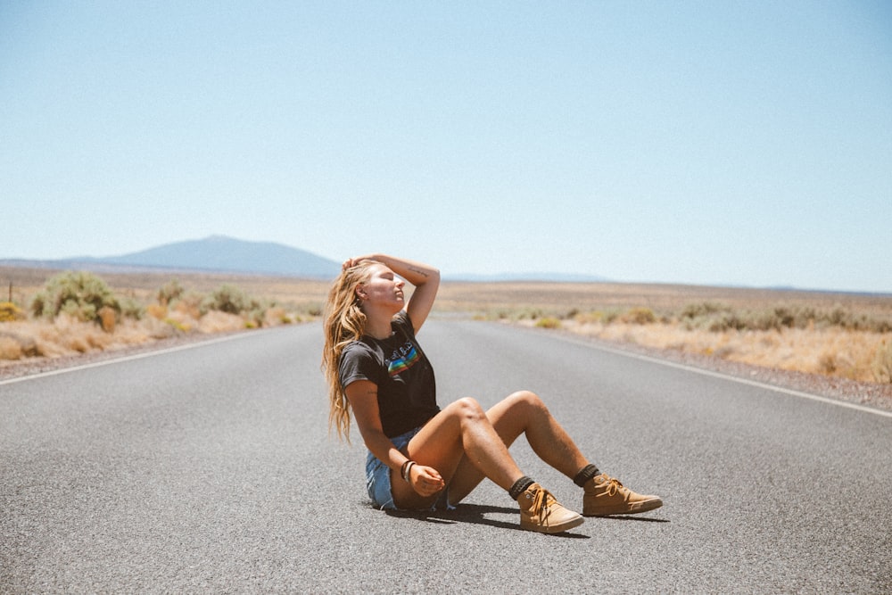 woman in black tank top and brown pants sitting on road during daytime