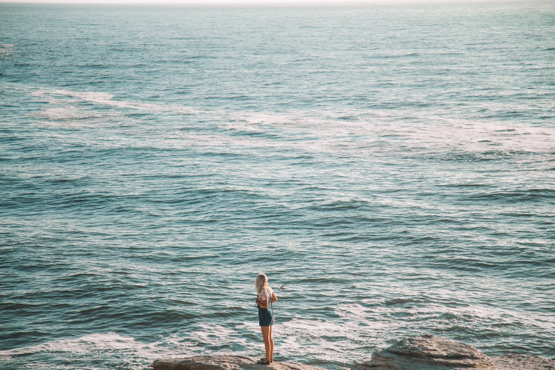 woman in white shirt and black shorts standing on sea shore during daytime