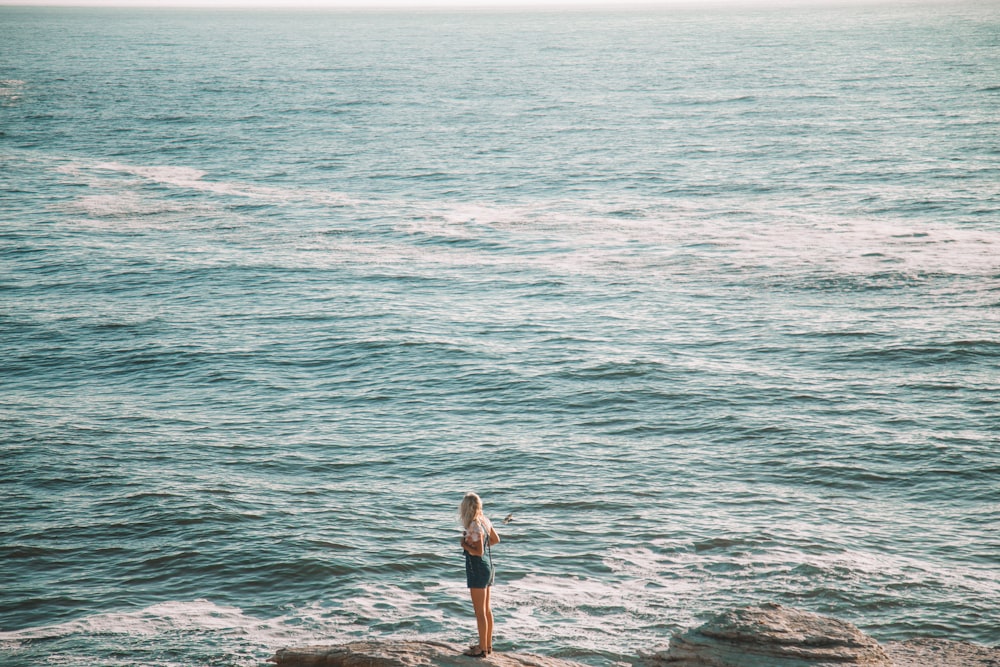 Mujer con camisa blanca y pantalones cortos negros de pie en la orilla del mar durante el día