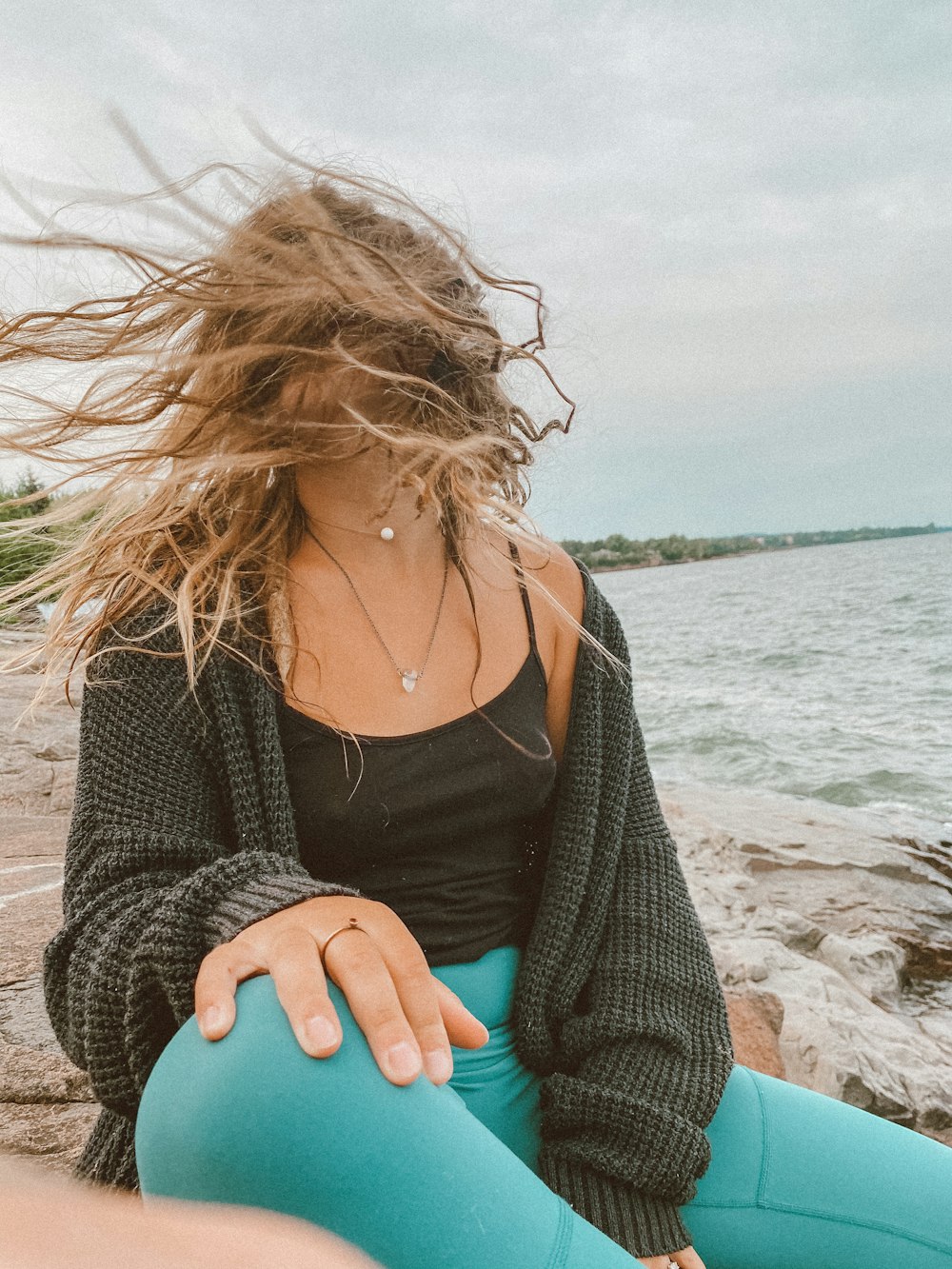 woman in black cardigan and blue denim jeans sitting on beach shore during daytime