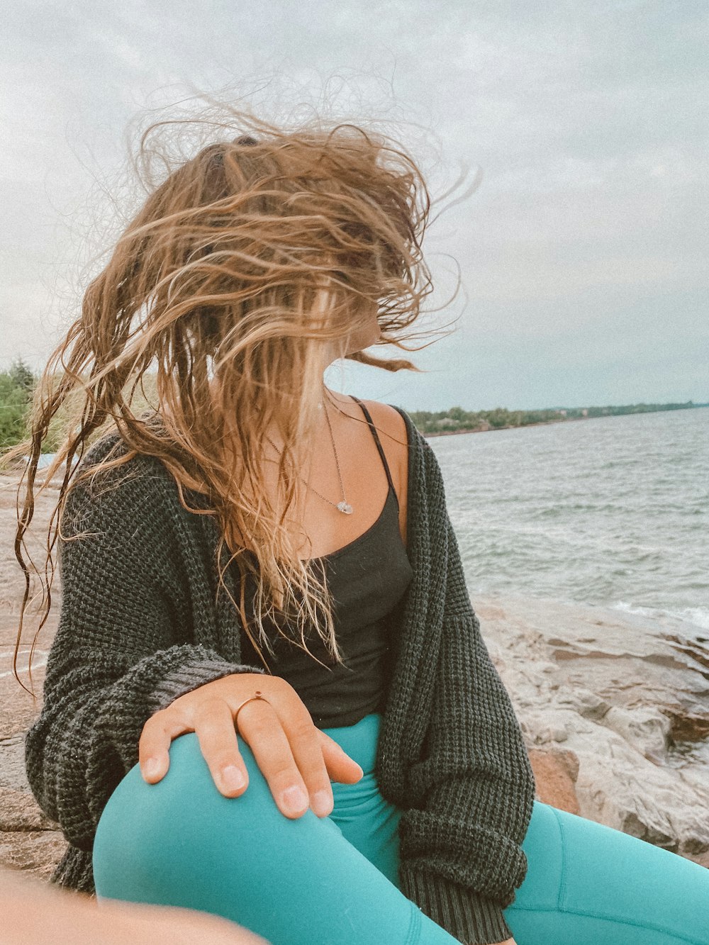 woman in black knit sweater sitting on beach shore during daytime