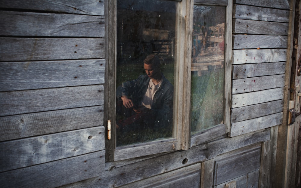 茶色の木枠のガラス窓の前に立つ黒いジャケットの男