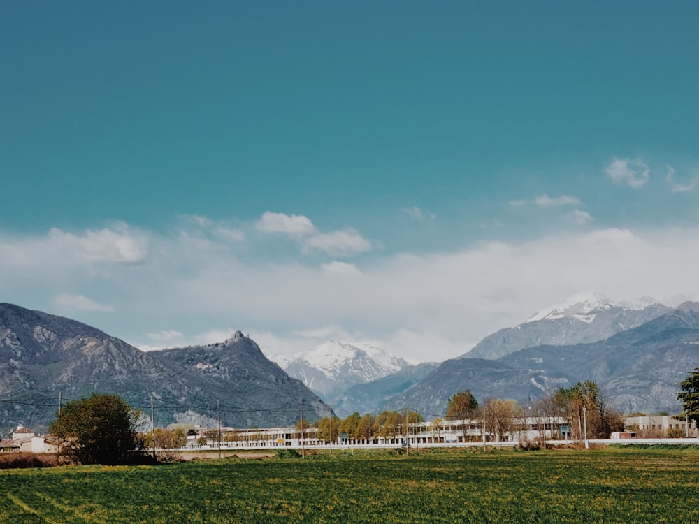campo di erba verde vicino alle montagne sotto il cielo blu durante il giorno