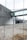 A metal fence is in the foreground with blurred view of a modern industrial or office building in the background. The structure features a metallic facade and a glass walkway connecting separate parts of the building. The area appears to be devoid of people.