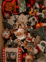 A collection of Christmas decorations is displayed, including plush reindeer, snowmen, and various ornaments. The decorations feature a festive theme with designs such as Christmas trees, stars, and snowflakes made from different materials including wood and fabric. Some of the ornaments are adorned with sequins and glitter, contributing to a festive and sparkling ambiance.