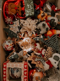 A collection of Christmas decorations is displayed, including plush reindeer, snowmen, and various ornaments. The decorations feature a festive theme with designs such as Christmas trees, stars, and snowflakes made from different materials including wood and fabric. Some of the ornaments are adorned with sequins and glitter, contributing to a festive and sparkling ambiance.