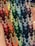 A collection of colorful, intricately woven friendship bracelets featuring geometric patterns. The designs incorporate a variety of colors, arranged in a repeating zigzag pattern, showcased against a person's palm, highlighting the handmade nature of the items.