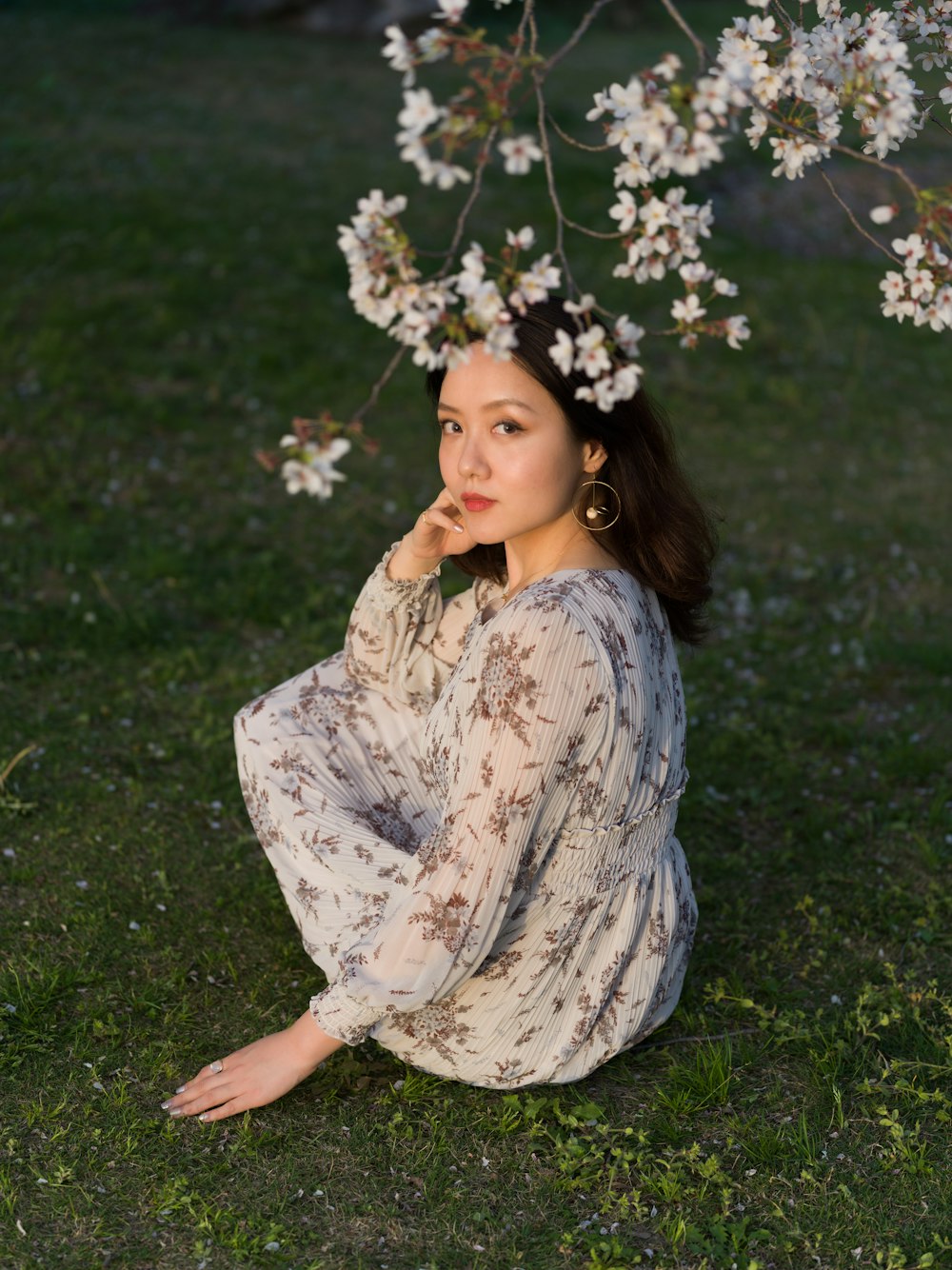 woman in white and blue floral dress sitting on green grass field