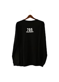 A black long-sleeve shirt is hanging on a wooden hanger. The text '705 CALIFORNIA' is printed in white on the back of the shirt.