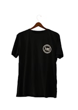 A black T-shirt hanging on a wooden hanger, featuring a circular emblem with the number '705' and the words 'seven zero five' twice around it.