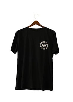 A black T-shirt hanging on a wooden hanger, featuring a circular emblem with the number '705' and the words 'seven zero five' twice around it.