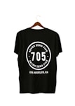 A black T-shirt is displayed on a wooden hanger with a bold white print on the back. The print includes the numbers '705' in large font, encased within a circular design. Above and below the numbers, the words 'SEVEN ZERO FIVE' and 'LOS ANGELES, CA' are printed respectively.