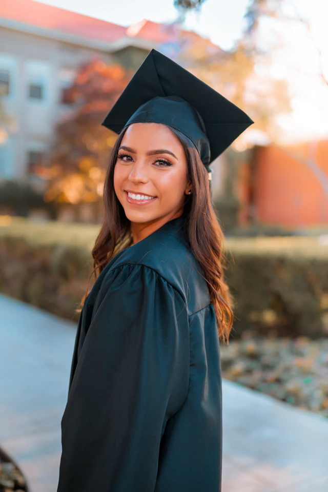 A smiling woman in a black graduation cap and gown outdoors