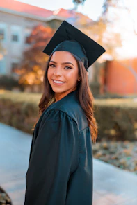 A smiling woman in a black graduation cap and gown outdoors