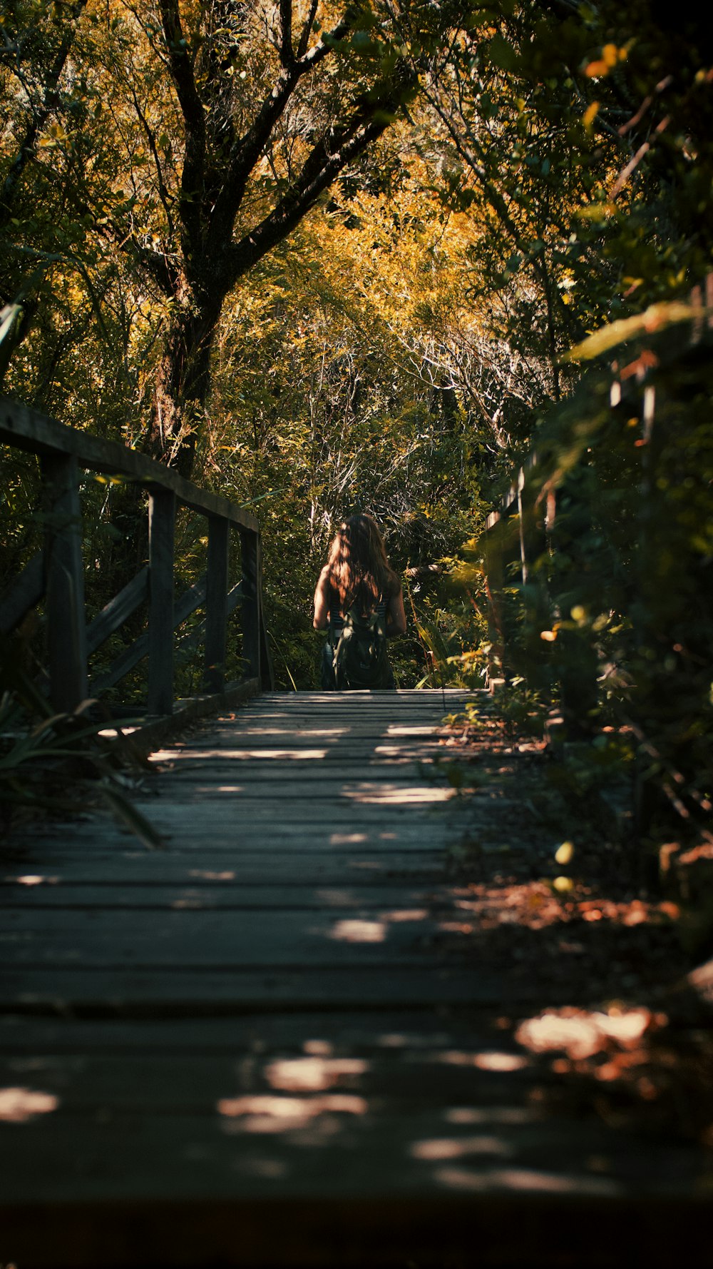 woman in black jacket walking on wooden bridge