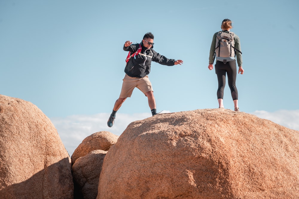 Hombre con chaqueta negra y pantalones cortos negros de pie en Brown Rock durante el día