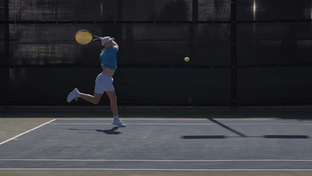 A dynamic tennis coach demonstrating a forehand stroke on a bright blue court under a clear sky.