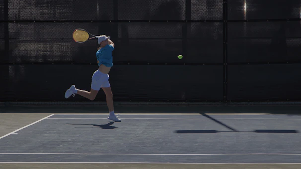 An action shot capturing a swift backhand stroke mid-swing on a clay court.