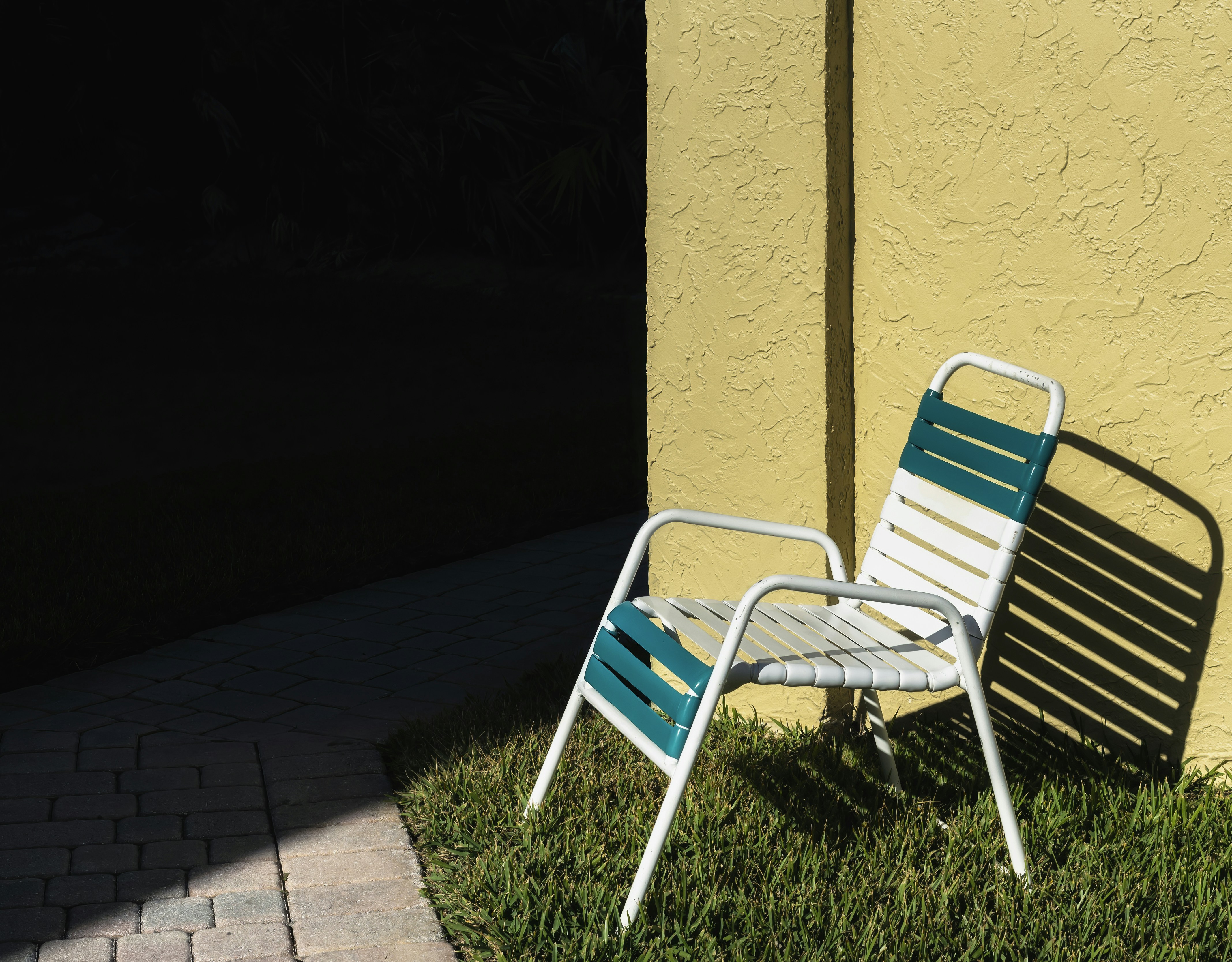 A striped chair sits on grass by a yellow wall.