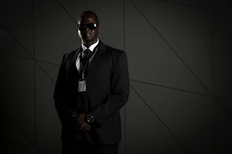 A vigilant security professional in a sleek black suit standing alert outside a luxury building at dusk.