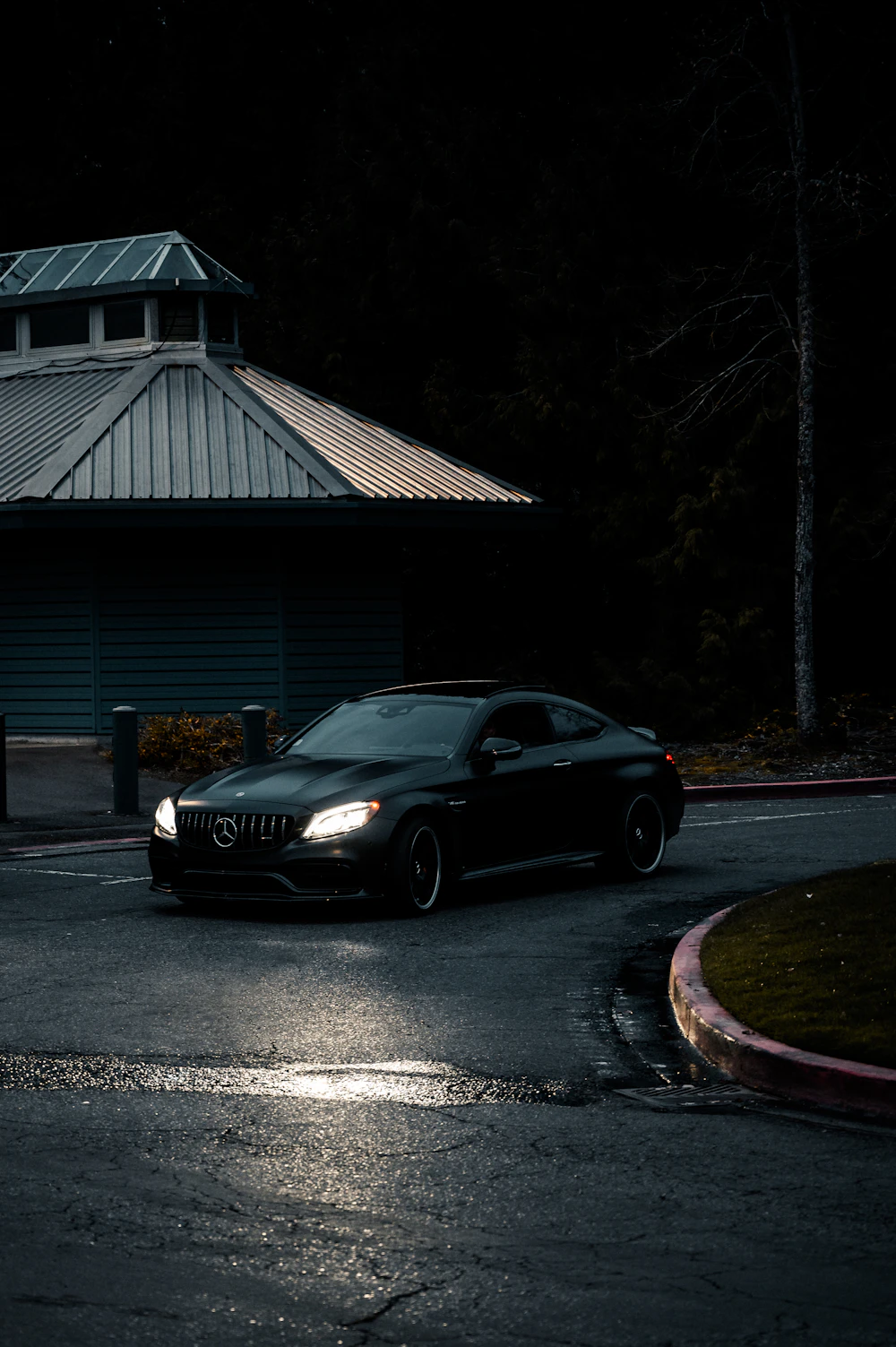 Black Mercedes with headlights on a wet road