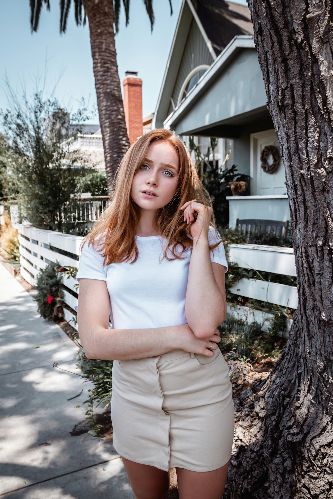 woman in white tank top and beige pants standing near brown wooden fence during daytime