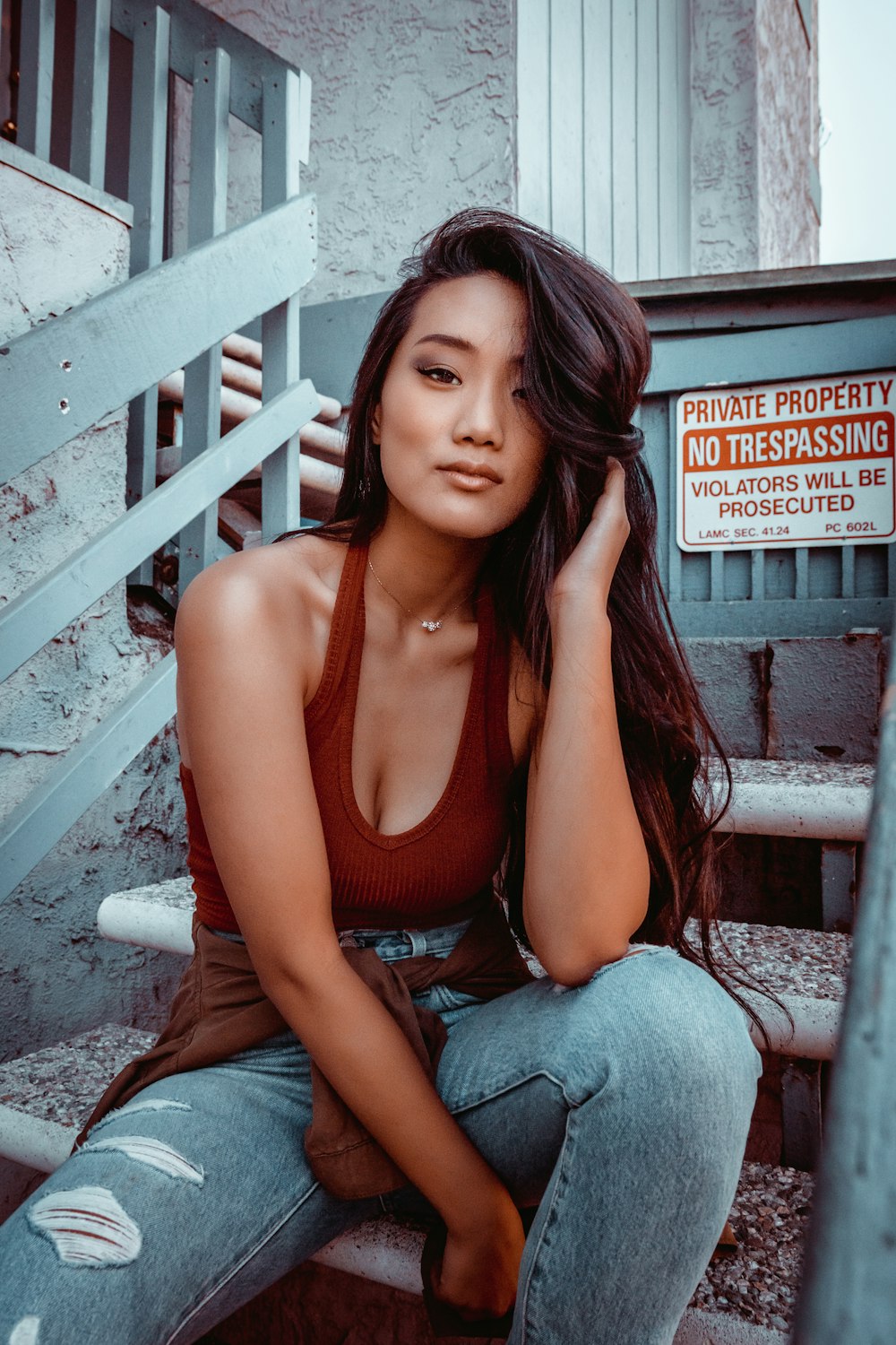 woman in red tank top and blue denim jeans sitting on gray wooden bench