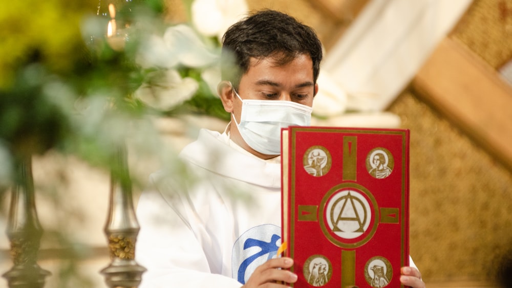 homem na camisa social branca segurando o livro vermelho