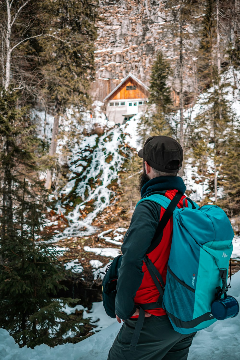 person in black and red jacket wearing black knit cap standing near brown wooden house during