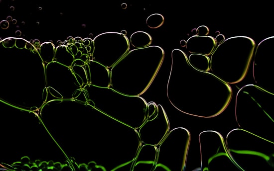 An arrangement of translucent bubbles interconnected and overlaying each other, illuminated with a green hue against a dark background. The shapes appear fluid and organic, resembling a network of abstract cells.