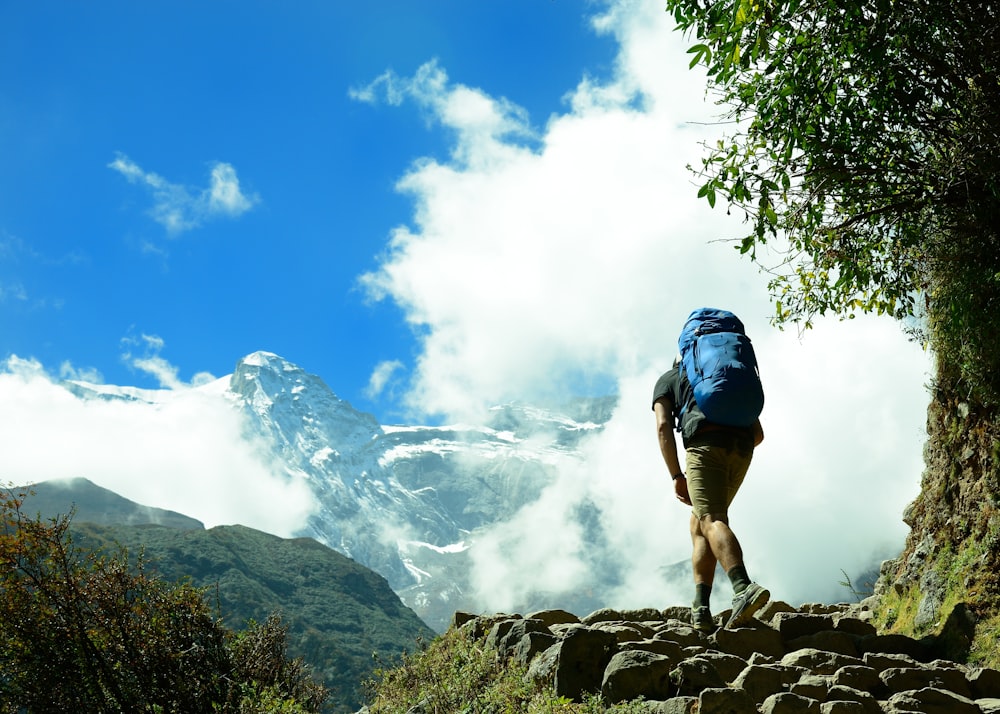 man in blue shirt and blue shorts standing on rocky mountain during daytime