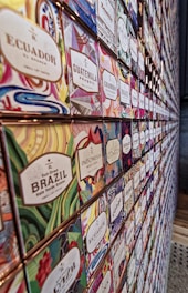 A wall displaying an assortment of colorful coffee packages, each labeled with different country origins such as Ecuador, Guatemala, Brazil, and others. The packages feature vibrant, abstract designs that are visually striking.