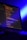 A computer screen displays lines of colorful code in a dimly lit room. The screen is angled to show the glowing text against a dark background, with blue ambient lighting creating a tech-focused atmosphere.