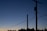 Silhouette of power lines and utility poles against a dusk or dawn sky with a gradient of deep blue to soft orange near the horizon. Trees are visible at the base, creating a contrast with the sky.