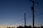 Silhouette of power lines and utility poles against a dusk or dawn sky with a gradient of deep blue to soft orange near the horizon. Trees are visible at the base, creating a contrast with the sky.