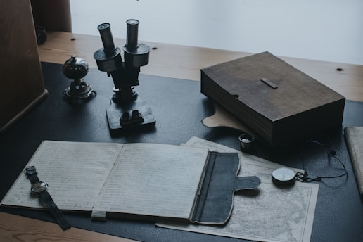 mesa de escritório, com cadernos, bússola, relógio e itens antigos de estudos