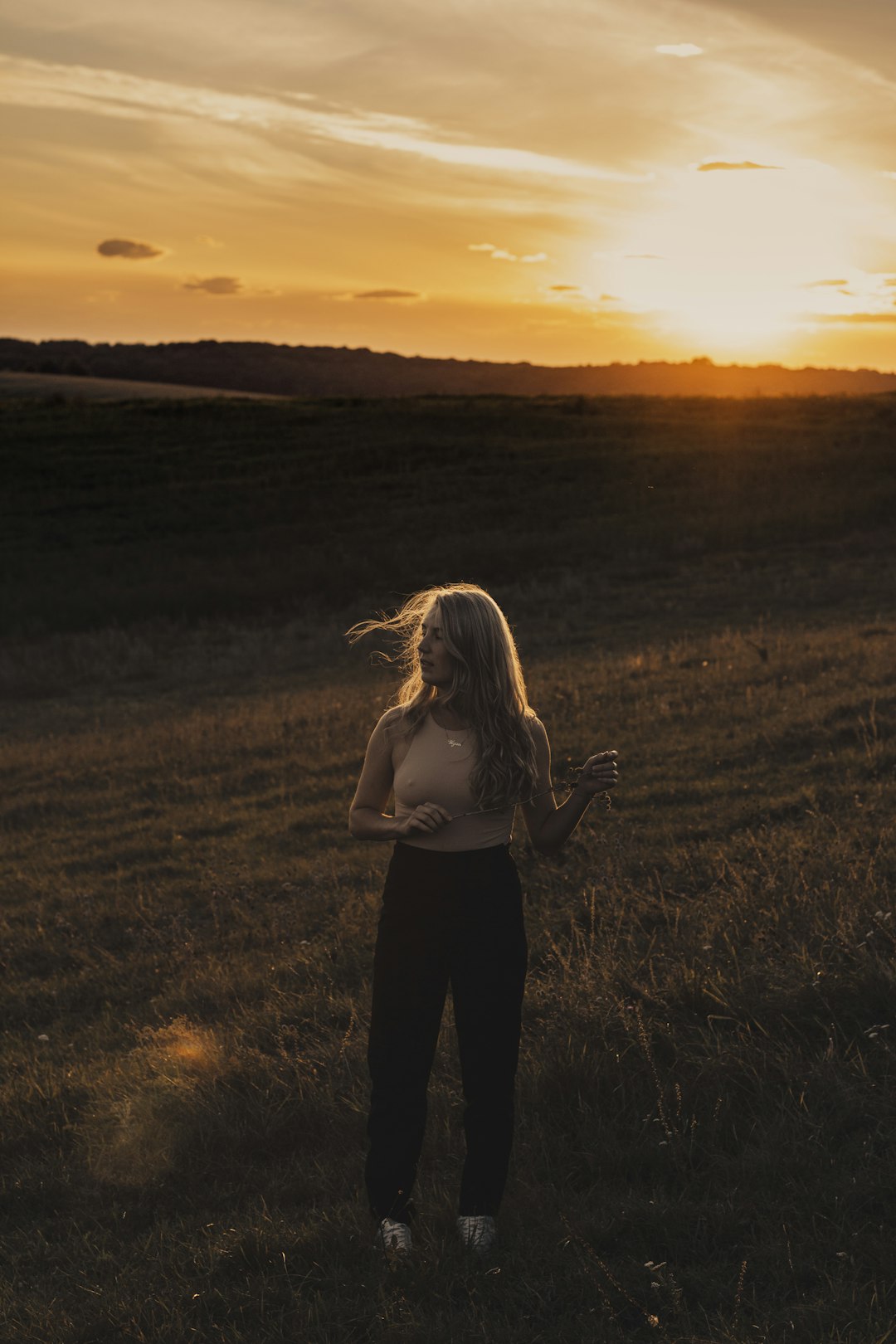 woman in white tank top and black pants standing on green grass field during sunset