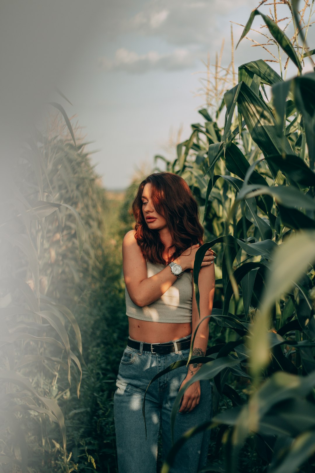 woman in black crop top and blue denim shorts standing in the middle of corn field