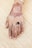 A henna design intricately applied on the back of a hand featuring floral patterns and calligraphy. The fingers are adorned with detailed henna art, and a black ring is worn on one of the fingers. The background consists of a textured bamboo mat.