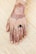 A henna design intricately applied on the back of a hand featuring floral patterns and calligraphy. The fingers are adorned with detailed henna art, and a black ring is worn on one of the fingers. The background consists of a textured bamboo mat.