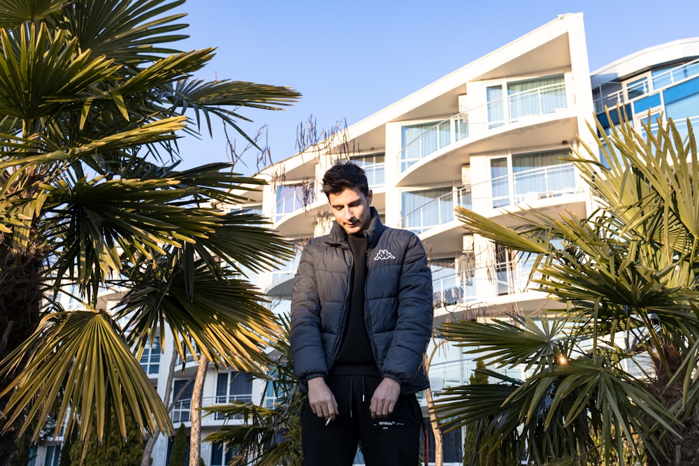 man in black suit jacket standing near palm tree during daytime