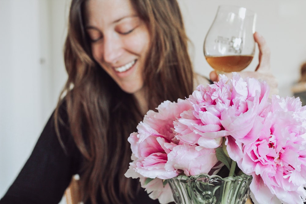 mulher na camisa preta da manga comprida que segura a flor cor-de-rosa