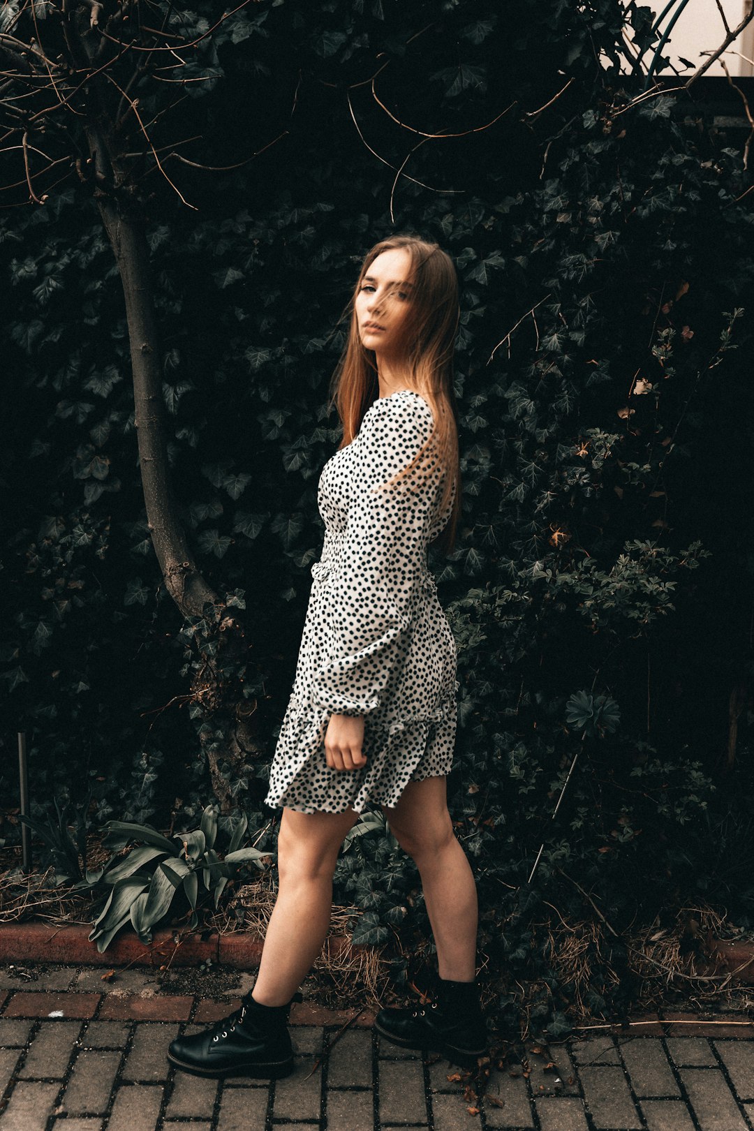 woman in black and white polka dot dress standing near green leaves