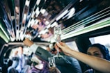 Inside a limousine, a group of people raising champagne glasses in a toast. The interior features reflective surfaces and green ambient lighting. The atmosphere suggests a celebratory occasion.