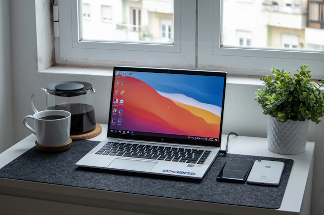 A sleek workspace with a laptop, notebook, and coffee cup, bathed in natural light.
