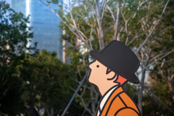 A cartoon figure wearing an orange coat and black hat is depicted against a backdrop of trees and a tall building. The figure is shown in profile, looking upwards.