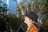 A cartoon figure wearing an orange coat and black hat is depicted against a backdrop of trees and a tall building. The figure is shown in profile, looking upwards.