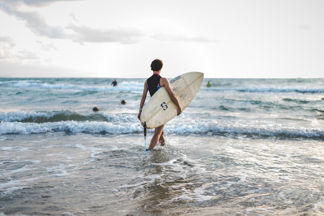 man in black wetsuit carrying white surfboard walking on beach during daytime