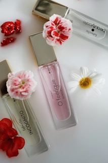 Three perfume bottles with elegant gold caps are arranged alongside vibrant red and white flowers on a sleek, white surface.